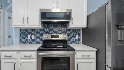 a kitchen with white cabinets and a stove and a microwave at Red Neptune by Nautical Properties in Panama City Beach