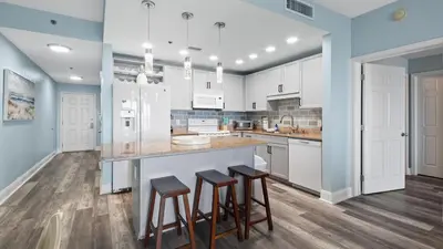 a kitchen with white cabinets and bar stools at Some Beach Some Where at Laketown Wharf #825 by Nautical Properties in Panama City Beach