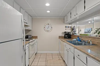 a kitchen with white cabinets and a sink and a refrigerator at Moondrifter #307 by Nautical Properties in Panama City Beach