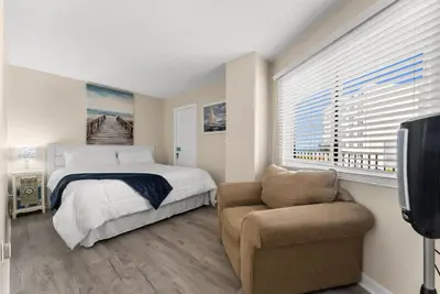 a bedroom with a bed and a chair and a tv at Moondrifter #307 by Nautical Properties in Panama City Beach