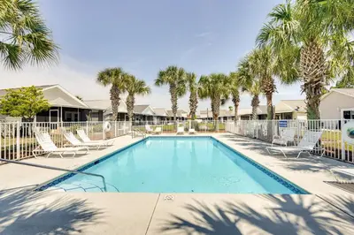 a swimming pool with chairs and palm trees at Panama City Vacation Rental with 2 Community Pools! in Panama City Beach