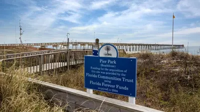 a sign on a beach with a pier in the background at A Salty Cru in Panama City Beach