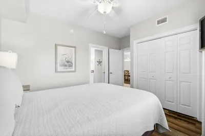 a white bedroom with a bed and a ceiling fan at Treasure Island #1008 in Panama City Beach