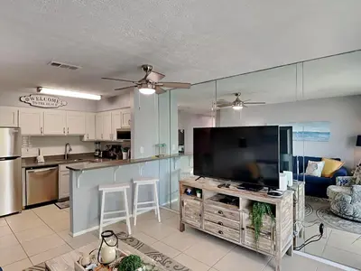 a living room with a large television and a kitchen at Endless Summer #A27 in Panama City Beach