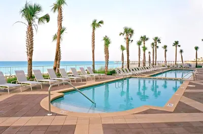 a pool with chairs and palm trees next to the ocean at Sterling Reef 1203 in Panama City Beach
