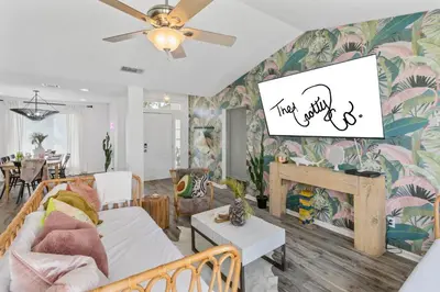 a living room with a couch and a tv on a wall at Steps to the beach & close to 30A! Private pool with sundeck & putt putt golf! in Panama City Beach