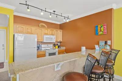 a kitchen with a white refrigerator and chairs at Ocean Reef 1106 - Lazy Daze in Panama City Beach