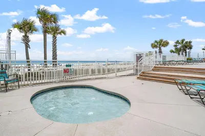 a small swimming pool with palm trees and the beach at Stunning 2/2 Designer Condo w Coastal Appeal Right on the Gulf! in Panama City Beach