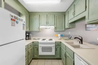 a kitchen with green cabinets and a white stove top oven at NEW! Steps To White Sand Beaches! Pool & Grill! 2BR 2BA in Panama City Beach
