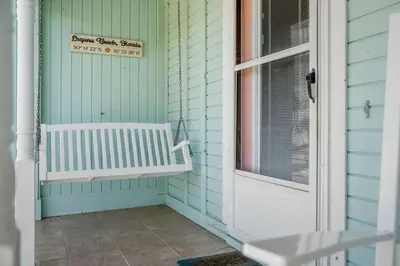 a porch with a white bench next to a door at NEW! Steps To White Sand Beaches! Pool & Grill! 2BR 2BA in Panama City Beach