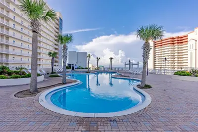 a swimming pool with palm trees and buildings at Luxury Gulf-View 3BD Condo! Free Beach Chairs! by Dolce Vita Getaways PCB in Panama City Beach