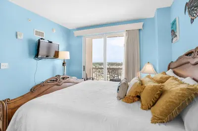 a bedroom with a large bed with blue walls and a window at Seychelles 1601 in Panama City Beach