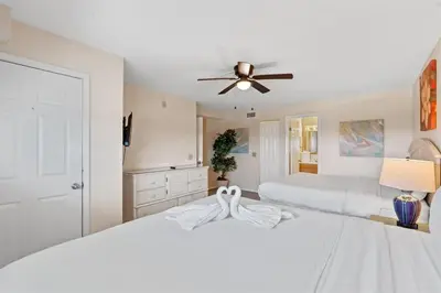 a white bedroom with two beds and a ceiling fan at The Summit 1512 in Panama City Beach