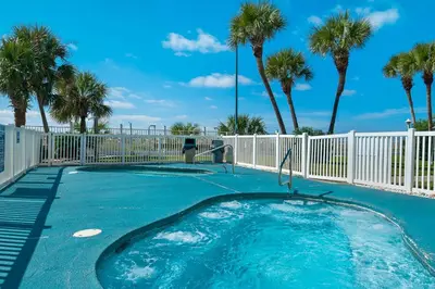 a swimming pool with palm trees and a fence at Beachfront - Beach Chairs Included! - FLPCB53 in Panama City Beach