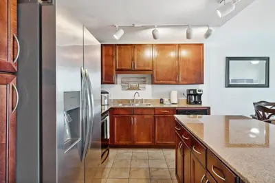 a kitchen with wooden cabinets and a stainless steel refrigerator at Remodeled 3BD plus Bunks! Low Floor Family Beach Resort! 5 Pools! by Dolce Vita Getaways PCB in Panama City Beach
