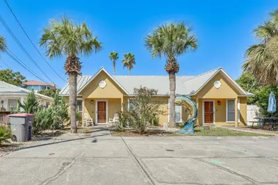 a yellow house with palm trees in front of it at Breezy PCB Vacation Rental with Lanai, Walk to Ocean in Panama City Beach