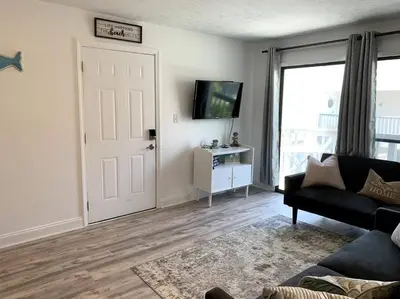 a living room with a couch and a tv and a door at FullyRenovated 1 min walk2 beach.5min to peir park in Panama City Beach