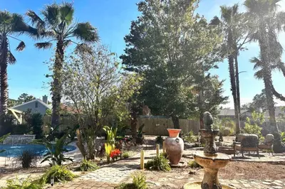 a garden with palm trees and a swimming pool at Shipwrecked - Private Pool Home, Game Room, 5 Min to Beach, Pets OK, & More! in Panama City Beach