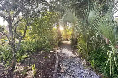a path through a garden with trees and plants at Shipwrecked - Private Pool Home, Game Room, 5 Min to Beach, Pets OK, & More! in Panama City Beach