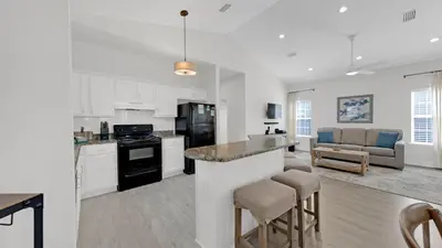 a kitchen and living room with white cabinets and a counter at Pelican House - Newly remodeled, professionally decorated, only about 1 mile to Seaside! in Santa Rosa Beach