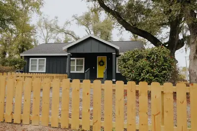 a black house with a yellow door behind a fence at Dream On – Style & Comfort Near Historic Downtown in Panama City