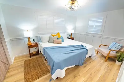 a bedroom with a bed and a chair and two windows at Conch Cottage in Panama City Beach