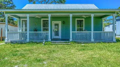 a green house with a porch and a yard at Flip Flop Cottage - Great rates and dog friendly with additional pet fee in Santa Rosa Beach
