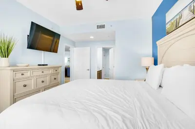 a white bedroom with a large bed and a flat screen tv at Sterling Reef 603 in Panama City Beach
