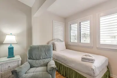 a bedroom with a bed and a chair and windows at PCB Townhome with Resort Amenities - Walk to Ocean! in Panama City Beach