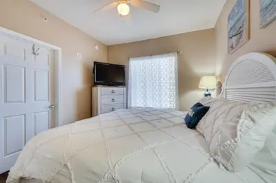 a bedroom with a white bed and a television at Panama City Beach Condo Balcony with Ocean Views! in Panama City Beach