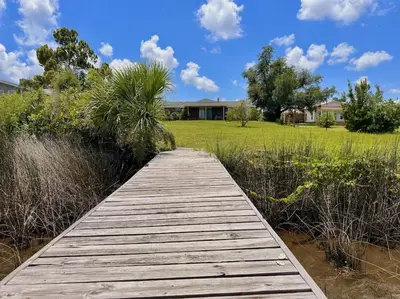 a wooden boardwalk over a field with a house at Nautical Nirvana-Waterfront Joys from Sunrise Paddles to Hot Tub Sunsets in Panama City