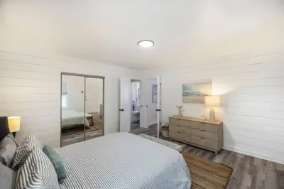 a white bedroom with a bed and a mirror at The Coastal Shanty, yards from the beach in Panama City Beach