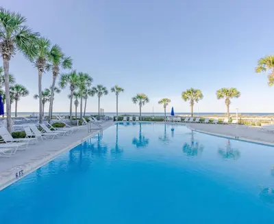 a large swimming pool with palm trees and a beach at Dunes of Panama Resort in Panama City Beach