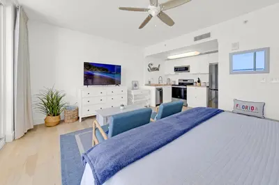 a white bedroom with a large bed and two blue chairs at Beachfront Studio #1112 at Majestic in Panama City Beach