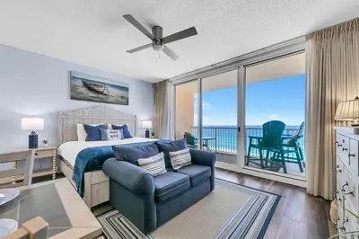 a bedroom with a bed and a chair and a balcony at Beachfront Studio #909 at Majestic in Panama City Beach