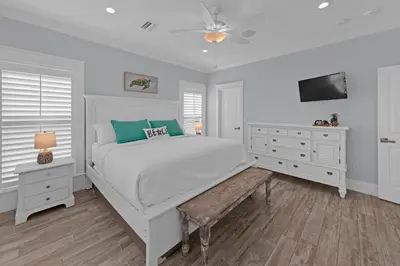 a white bedroom with a white bed and a tv at Sea Suite - Large hot tub with an easy walk to the beach in Santa Rosa Beach