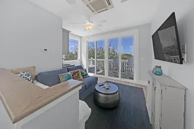 a living room with a blue couch and a tv at Sea Suite - Large hot tub with an easy walk to the beach in Santa Rosa Beach