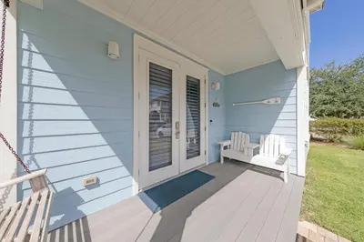 a porch of a blue house with two white chairs at Sea Suite - Large hot tub with an easy walk to the beach in Santa Rosa Beach