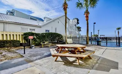 a picnic table in front of a building with palm trees at Sunbird Resort! Incredible Beachfront Corner Unit! Free Beach Chairs! by Dolce Vita Getaways PCB in Panama City Beach