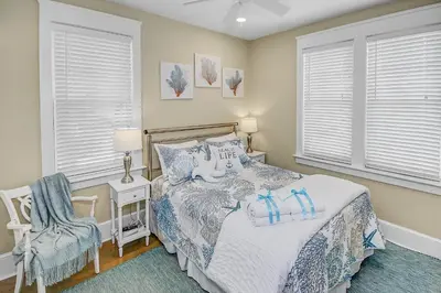 a bedroom with a bed and a chair and windows at Almost Heaven in Watersound Proper INCLUDES Carriage House! Bedding for 12 in Rosemary Beach