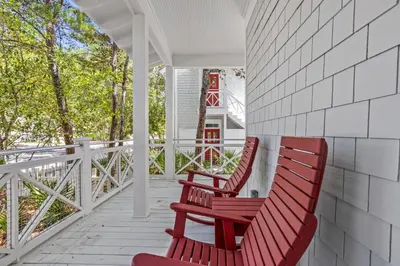 two red chairs sitting on the porch of a house at Almost Heaven in Watersound Proper INCLUDES Carriage House! Bedding for 12 in Rosemary Beach