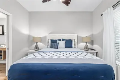 a white bedroom with a blue bed and two lamps at Splash Resort Beachfront in Panama City Beach