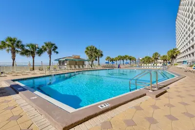 a swimming pool next to a beach with palm trees at Steps to Shore PCB Condo with Pool Access and Views! in Panama City Beach