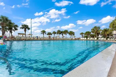 a swimming pool with palm trees and a blue sky at The Summit 518 in Panama City Beach