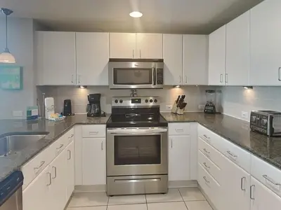 a kitchen with white cabinets and a stove and a microwave at Grand Panama Beach Resort - The Grand #201 - Sunny Shores in Panama City Beach