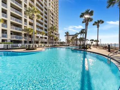 a large swimming pool with palm trees in front of a building at Grand Panama Beach Resort - The Grand #201 - Sunny Shores in Panama City Beach