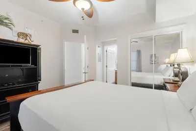 a white bedroom with a bed and a tv at Seychelles #703 by Nautical Properties in Panama City Beach
