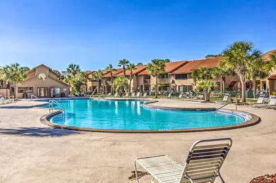 a swimming pool at a resort with chairs and palm trees at Walk to Beach and Restaurants PCB Resort Condo! in Panama City Beach