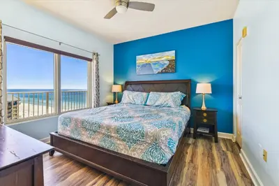 a bedroom with a bed with a blue wall and a window at Shores of Panama 1427 condo in Panama City Beach