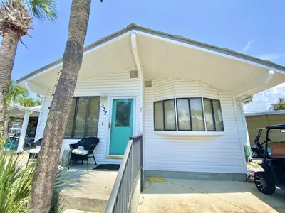 a white house with a porch and a palm tree at Venture Out 332 Lagoon Ln WITH 2 GOLF CARTS in Panama City Beach